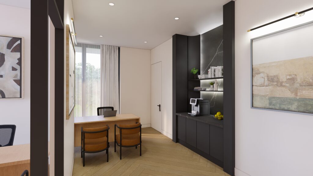 Modern office space with two tan chairs at a wooden desk, a small kitchenette area with shelves, a coffee maker, and decorative items. Large window with sheer curtains and framed artwork on the walls.