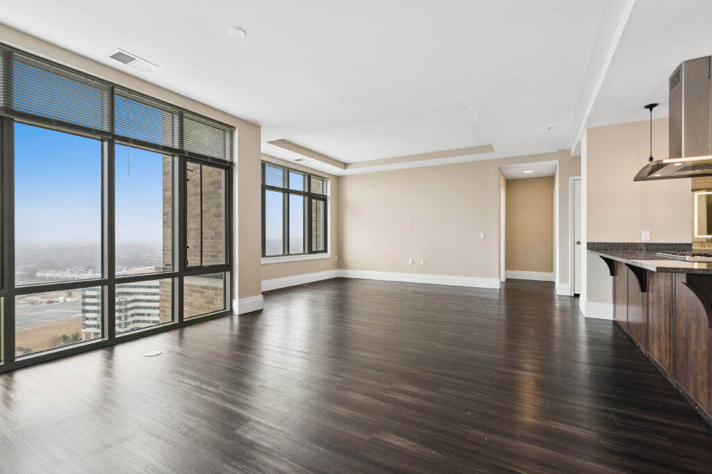 Spacious, modern apartment with dark wood floors, large floor-to-ceiling windows offering city and river views, an open layout, and a kitchen area with granite countertops and stainless steel appliances.